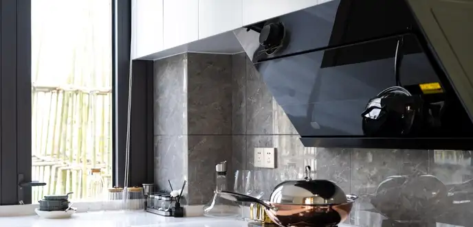 Modern kitchen with a black extractor hood made of glass, sleek white countertops, a gas glass hobtop, and various kitchen utensils near a large window