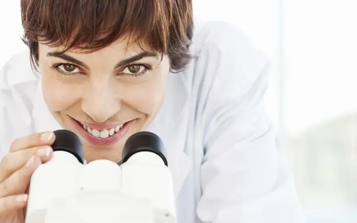 Female looking up from a stereo microscope in a laboratory