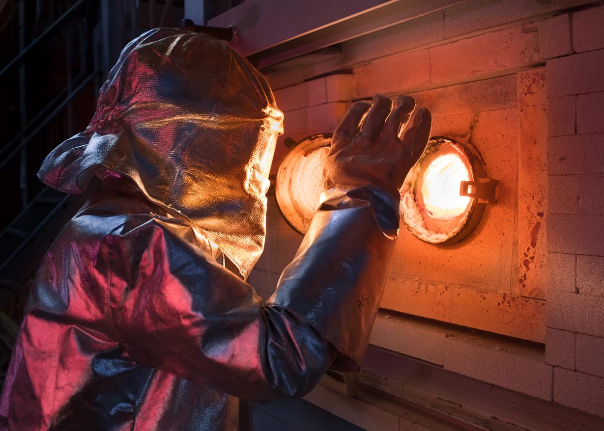 Man in protective suit, view into glass melting tank