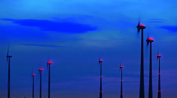 Series of wind turbines with red LED beacon lights at dusk