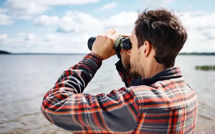 Man looking through binoculars across lake