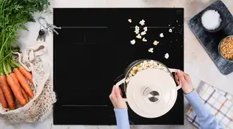 Top view of a SCHOTT CERAN® Miradur cooktop with a cooking pot, popcorn, keys and fresh ingredients in a kitchen setting. 