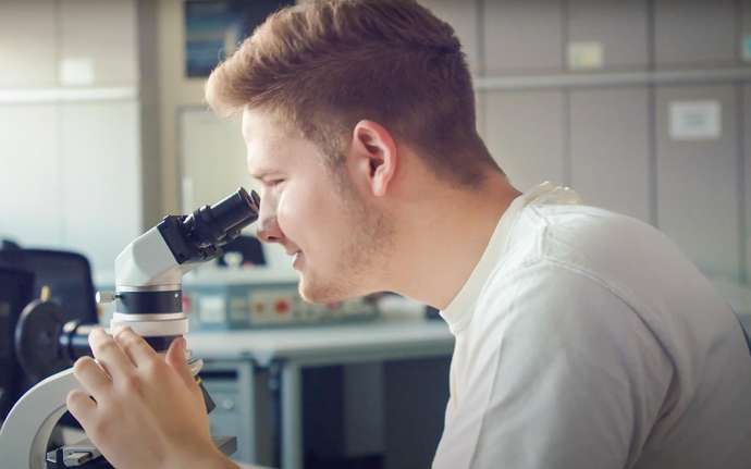 Junger SCHOTT Auszubildender beim Blick ins Mikroskop