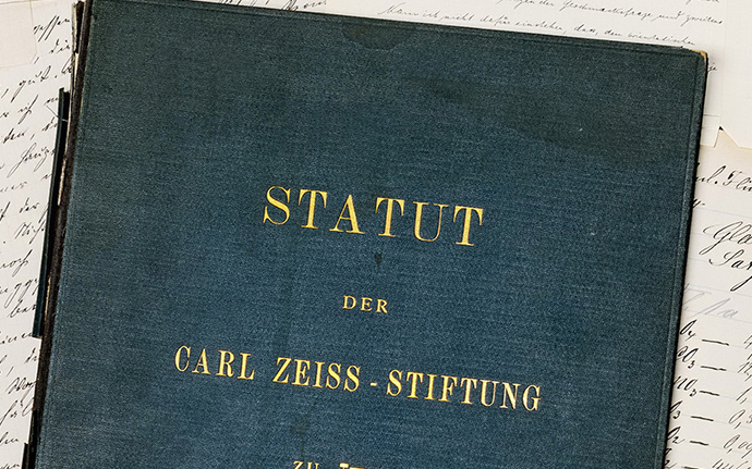 Ein historisches Buch mit dem Titel „Statut der Carl Zeiss‑Stiftung“ liegt auf handschriftlichen Dokumenten.