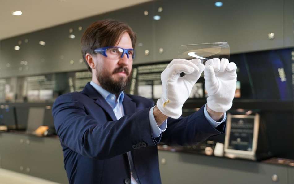 A man wearing safety glasses folds a flexible UTG glass sample.