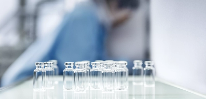 Glass vials arranged on a laboratory table with a blurred figure in the background.