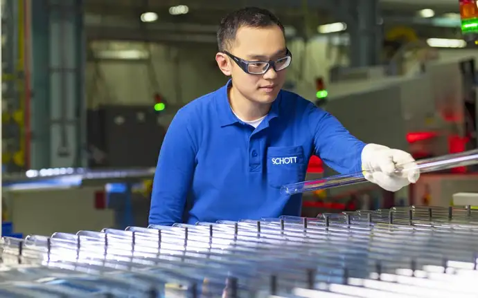 Man with protective clothing in front of pharmaceutical tube production, Holding a pharmaceutical glass tube in his hand.