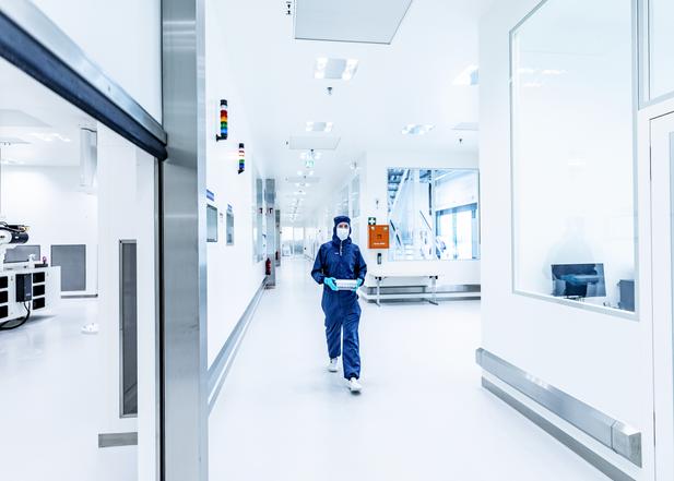 A woman in a protection suit walks through a lab.