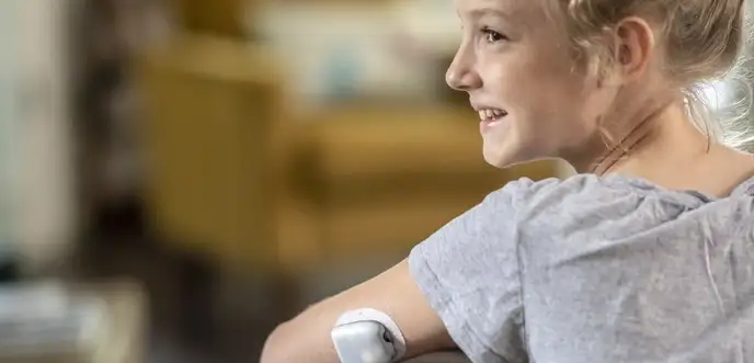 Child sitting on a chair smiling with on-body deliver system attached to arm.