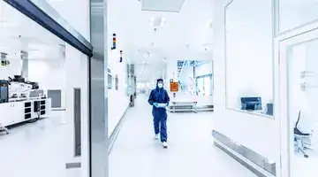 A technician in a cleanroom suit walks through a sterile laboratory