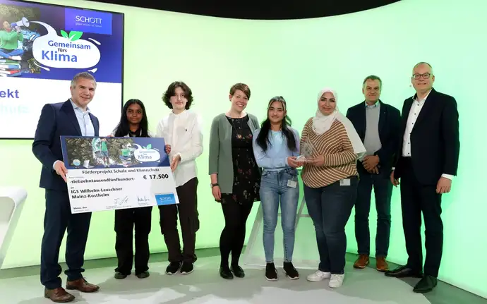 Two SCHOTT business executives present a check to a group of teachers and students from Mainz, Germany