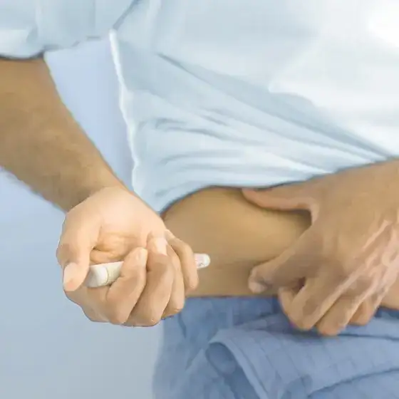 Hombre inyectándose medicamentos en el estómago con un autoinyector