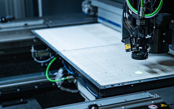 Eine hochpräzise industrielle Maschine mit grünen Kabeln arbeitet über einer großen, flachen Arbeitsfläche.