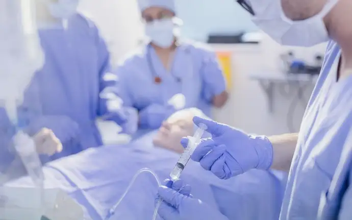 Anesthetist with a syringe injecting anesthetic into IV drip in the operating room