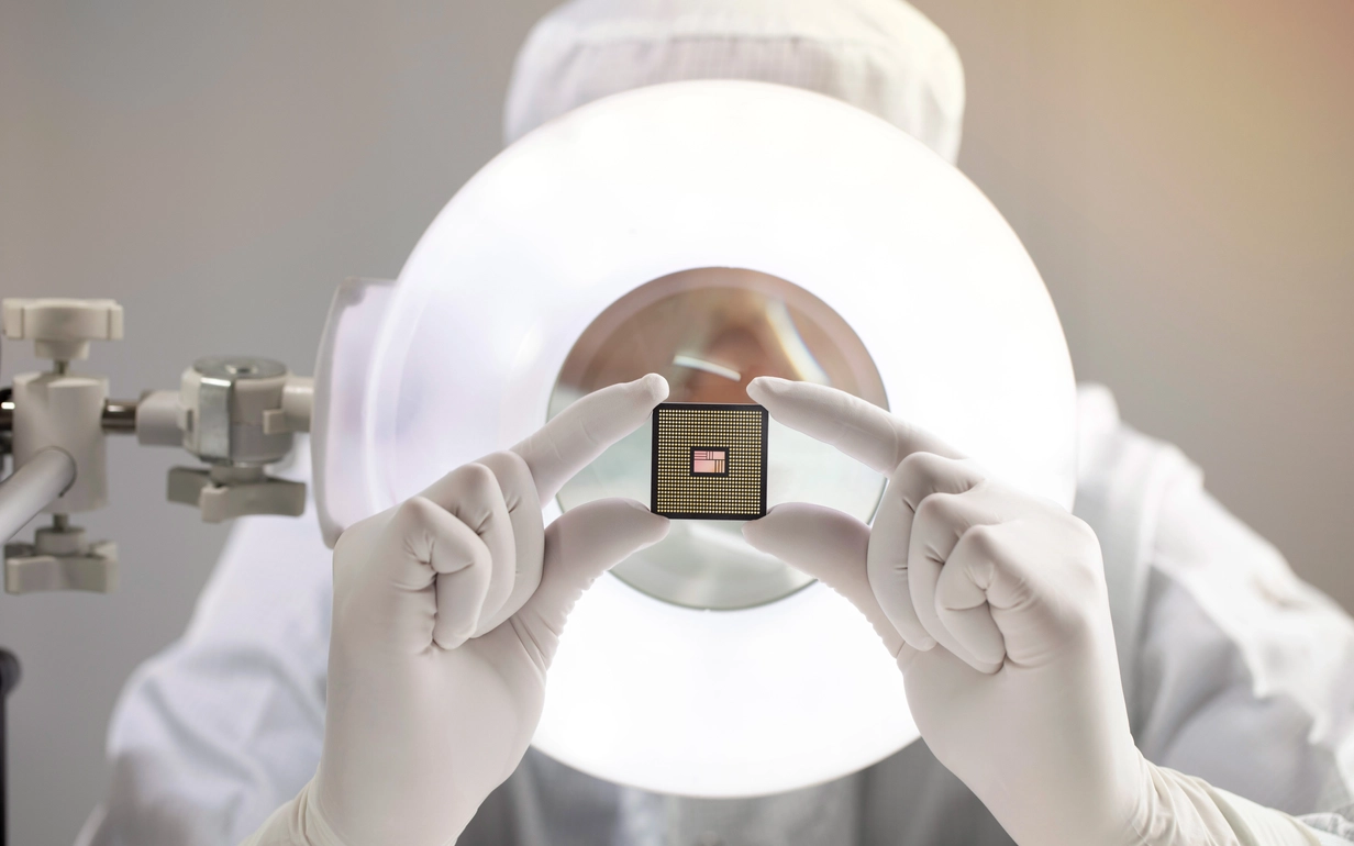 Person in cleanroom clothing testing a microchip for the semiconductor industry.