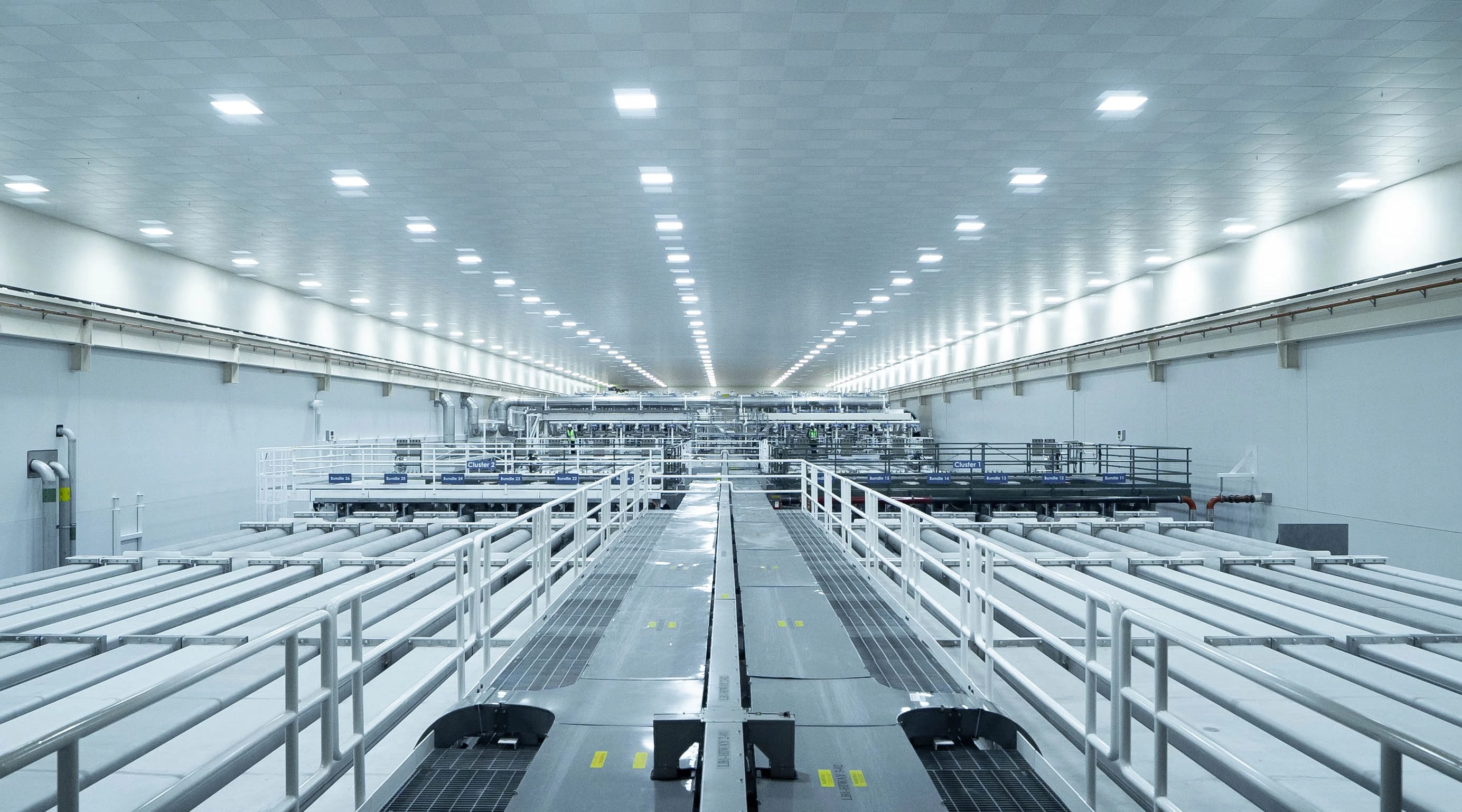 A massive white room with long pipes and walkways extending as far as the eye can see.