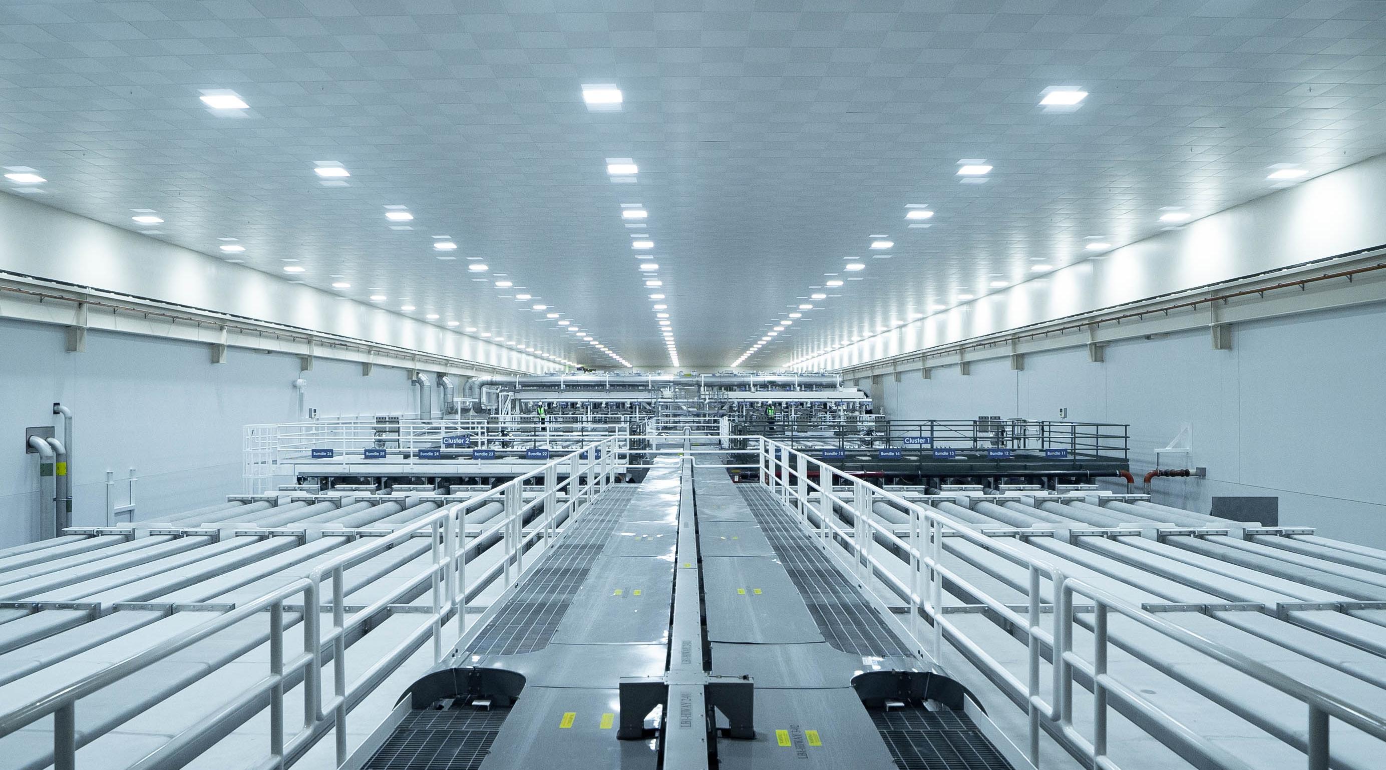A massive white room with long pipes and walkways extending as far as the eye can see.