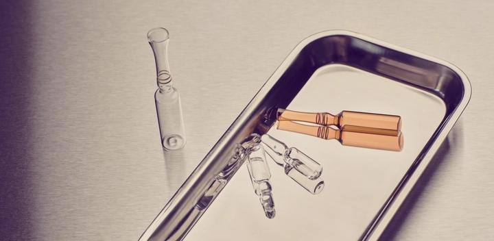 Glass ampoules, including two amber ones, arranged on a metal medical tray