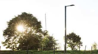 A solar-powered street light with tree and sun in background