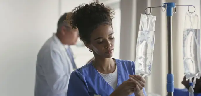 Female nurse adjusts IV equipment with clinician in background