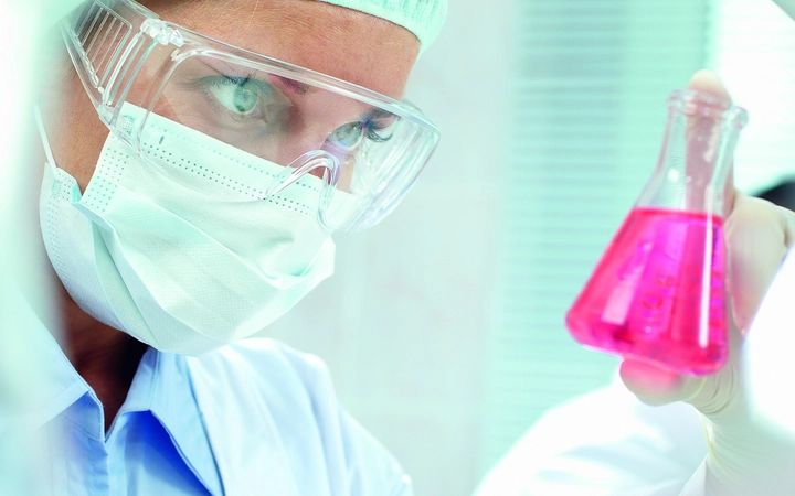 Scientist in glasses and face mask looks at a red liquid 