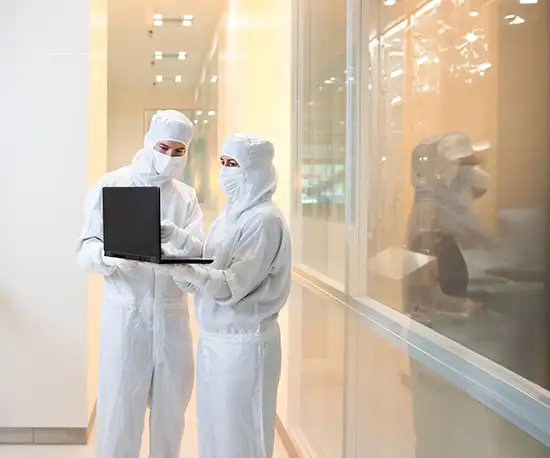 Zwei Personen in weißer Reinraumbekleidung stehen nebeneinander und betrachten gemeinsam einen geöffneten Laptop.