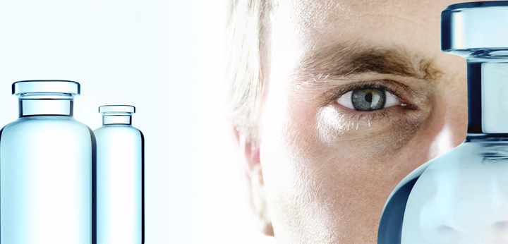 Man looking at three clear pharmaceutical glass vials made by SCHOTT Pharma