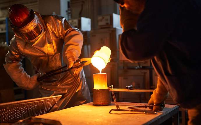 Worker in heat protection suit pours molten glass into a mould