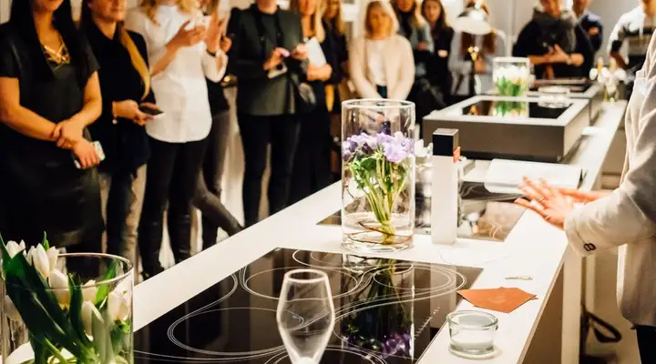 People standing around various SCHOTT CERAN® glass-ceramic cooking surfaces during a live presentation