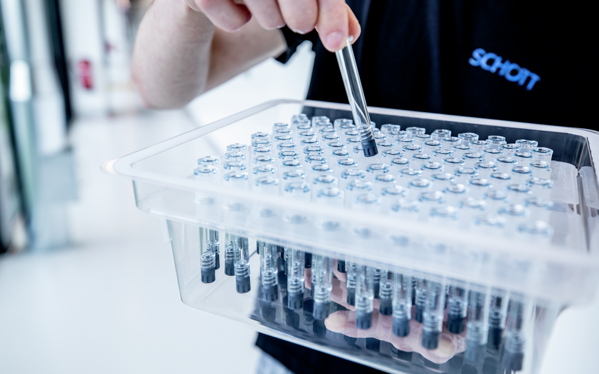 A SCHOTT employee holds a prefillable polymer syringe above a nest and tub.