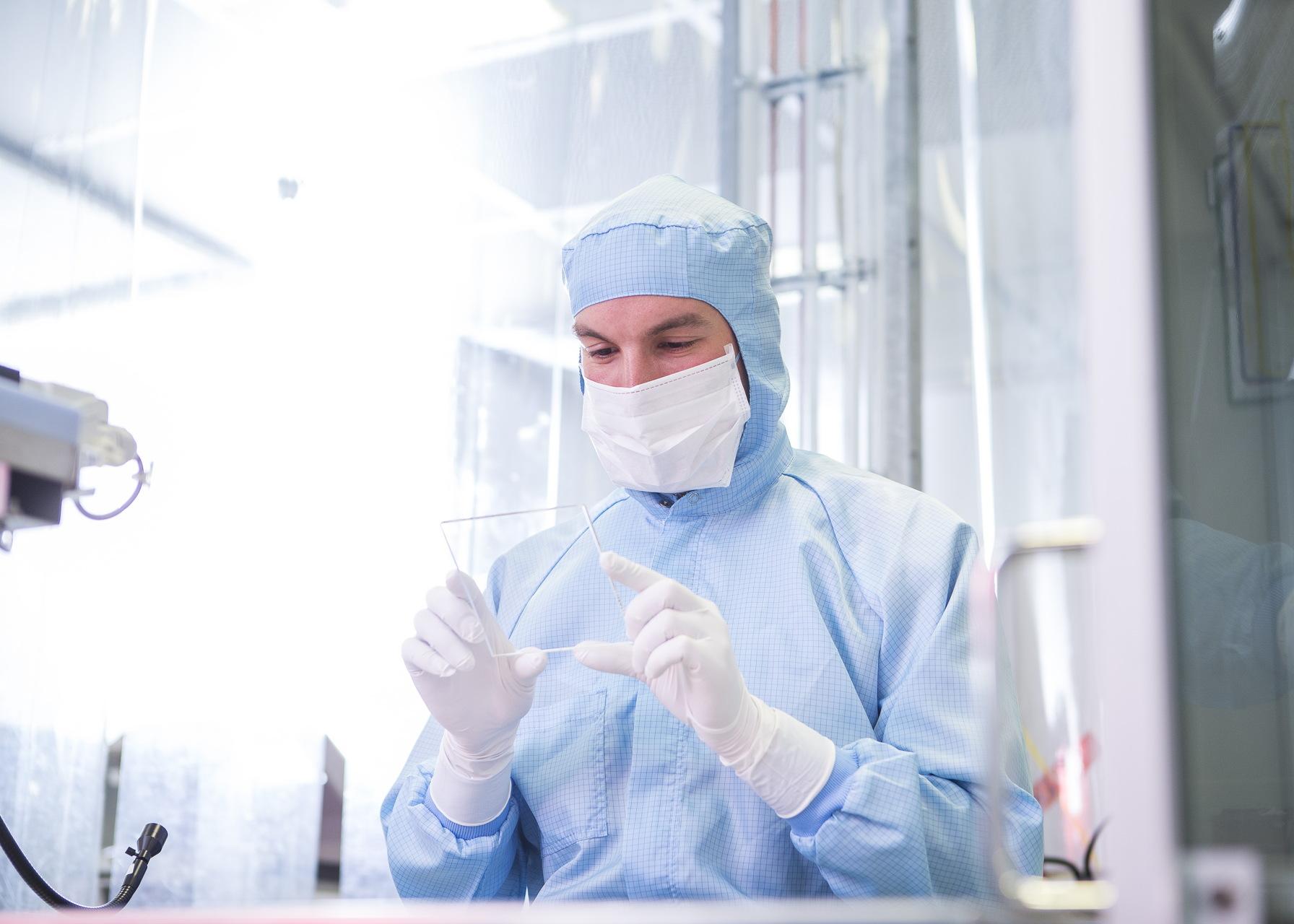 Laboratory scientist in cleanroom clothing inspects a glass sample