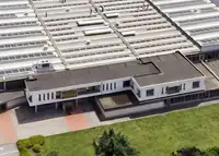 Aerial view of a large industrial manufacturing facility with multiple roof sections covered in skylights and solar panels, surrounded by greenery.