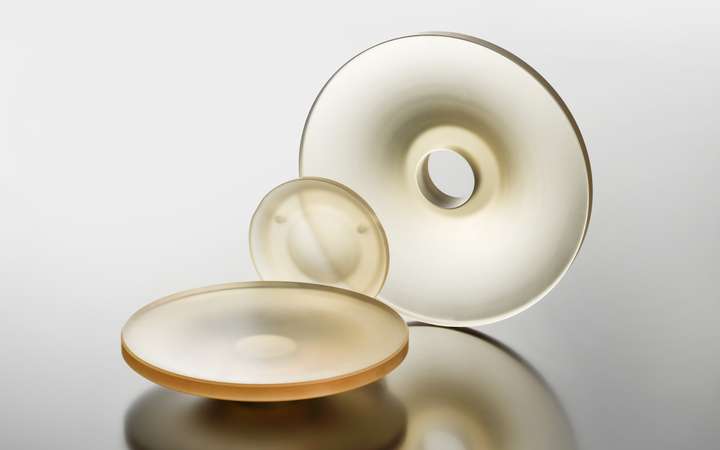 Three glass-like objects of varying sizes with smooth surfaces and circular shapes arranged together on a reflective surface.