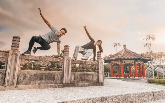 Male and female jump over a low wall together