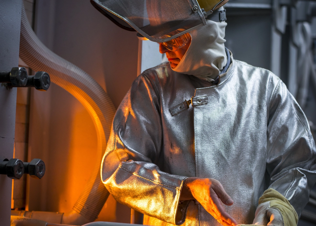 Man in protective suit looking into the melting tank