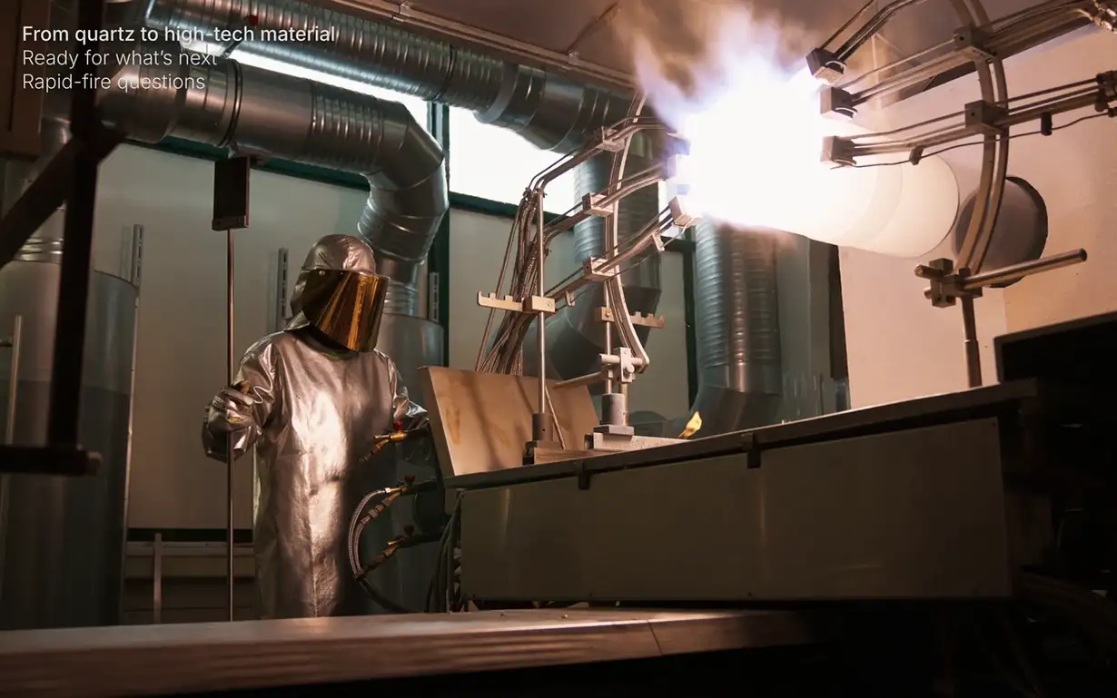 A person in a protective suit operates machinery in an industrial setting with bright light and ductwork visible in the background.