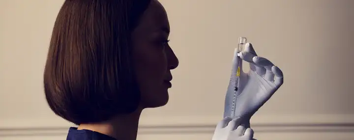 Side profile of a clinician in gloves holding a vial and syringe.