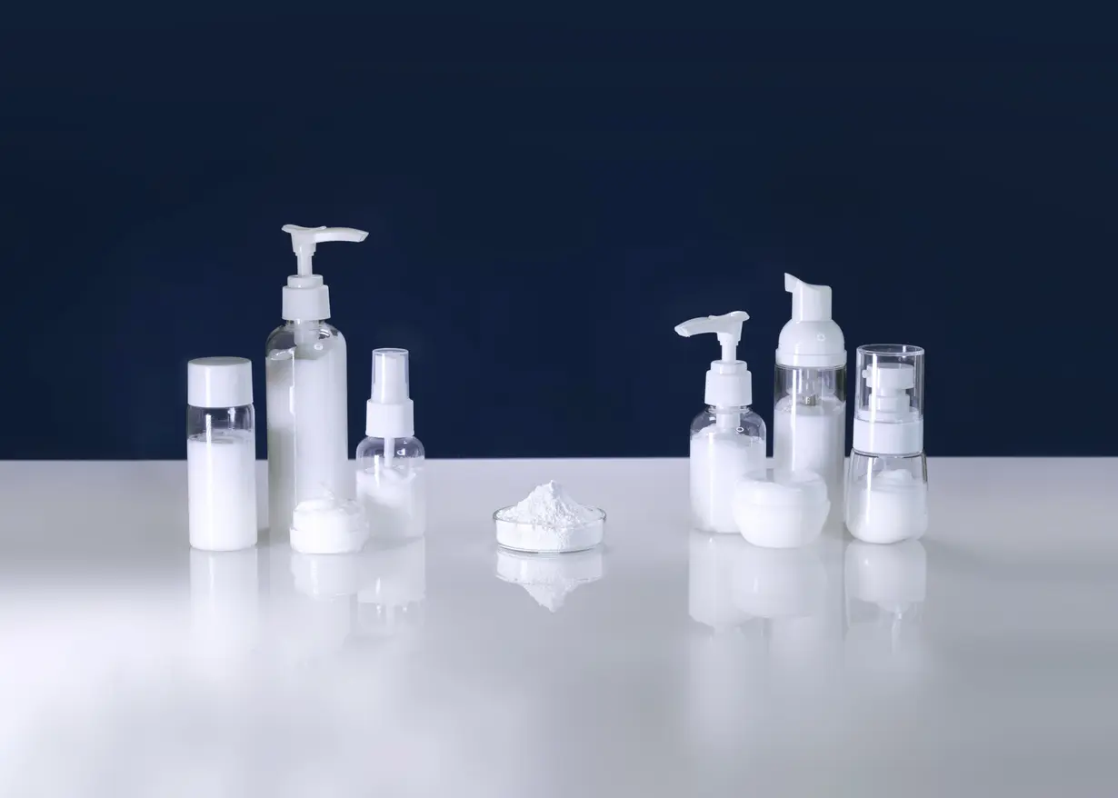 Various white cosmetic bottles and -dispensers on a white worktop against a black background.