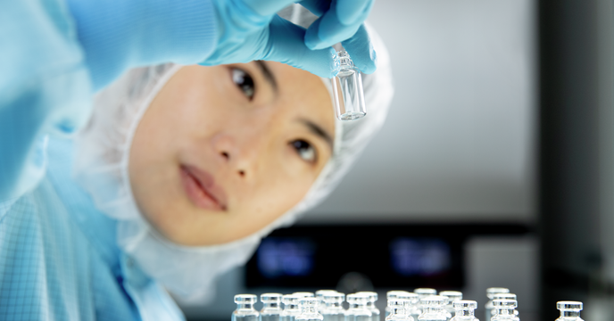 Women in clean room clothing looking at vial