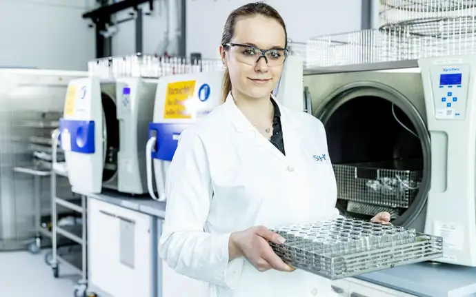 Woman in the laboratory wearing safety goggles and a white lab coat holding a nest of pharmaceutical vials.