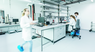 Female technician walks across a laboratory with colleagues in background