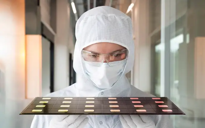 A woman in cleanroom attire is holding a tray of substrates
