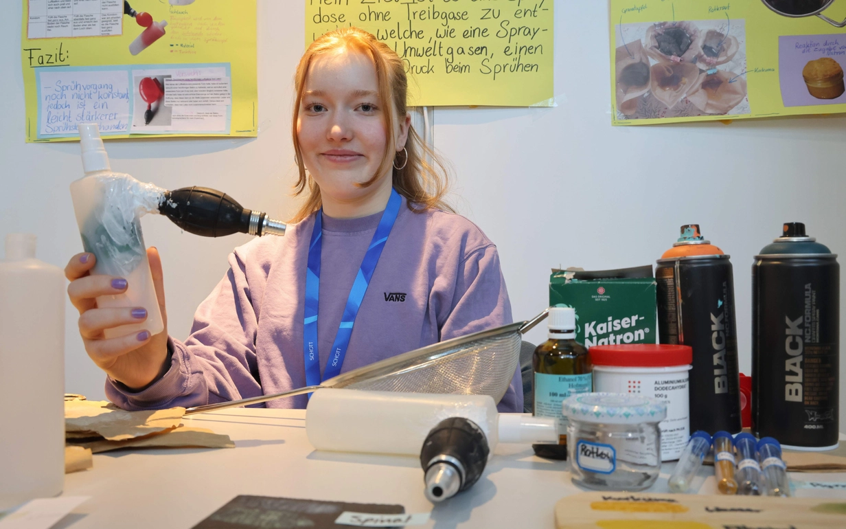Mia Schubert hält eine Spraydose ohne Treibgase in der Hand, bei der mithilfe eines Luftballons und einer Handpumpe konstanter Druck erzeugt wird.