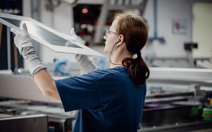 A woman in a production line checks glass panes for visual defects.