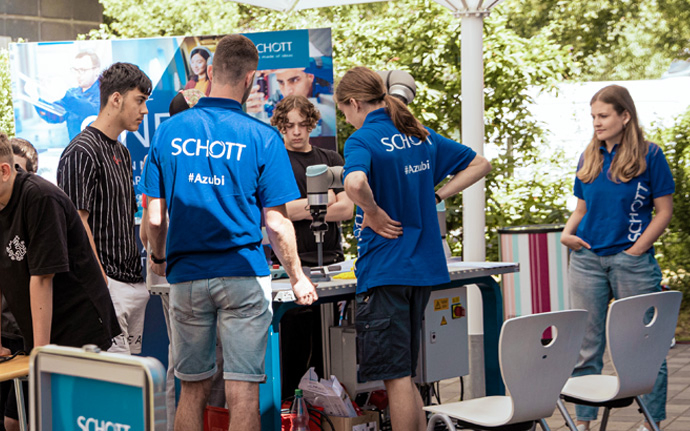 Mehrere Personen in blauen SCHOTT‑Shirts stehen an einem Infostand im Freien und führen Gespräche.