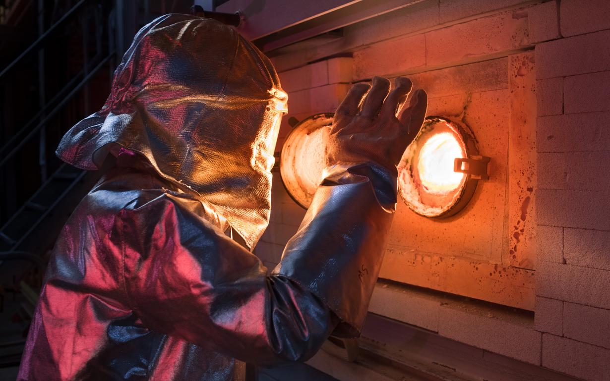 Man in heat protective clothing looks into the melting tank.