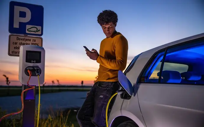 Ein Mann verwendet ein Handy, während er wartet, bis sein Elektroauto an der Ladestation geladen wird