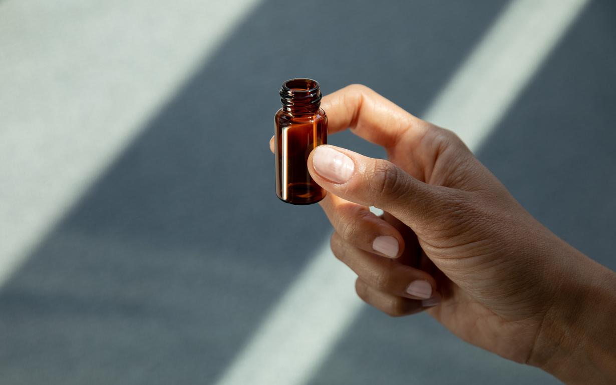 A hand holding a glass vial made of amber borosilicate glass