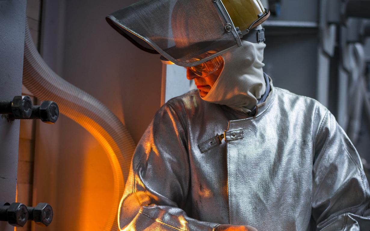 SCHOTT employee in protective gear looks at the glass furnace