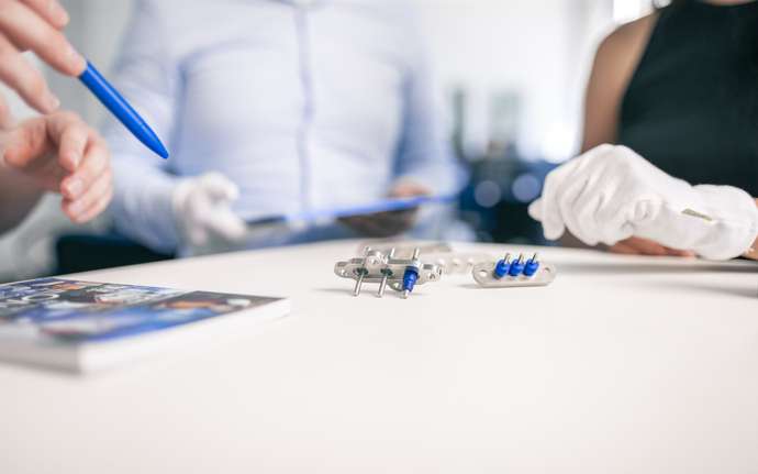 Gloved hands handling compressor terminals on a white table.